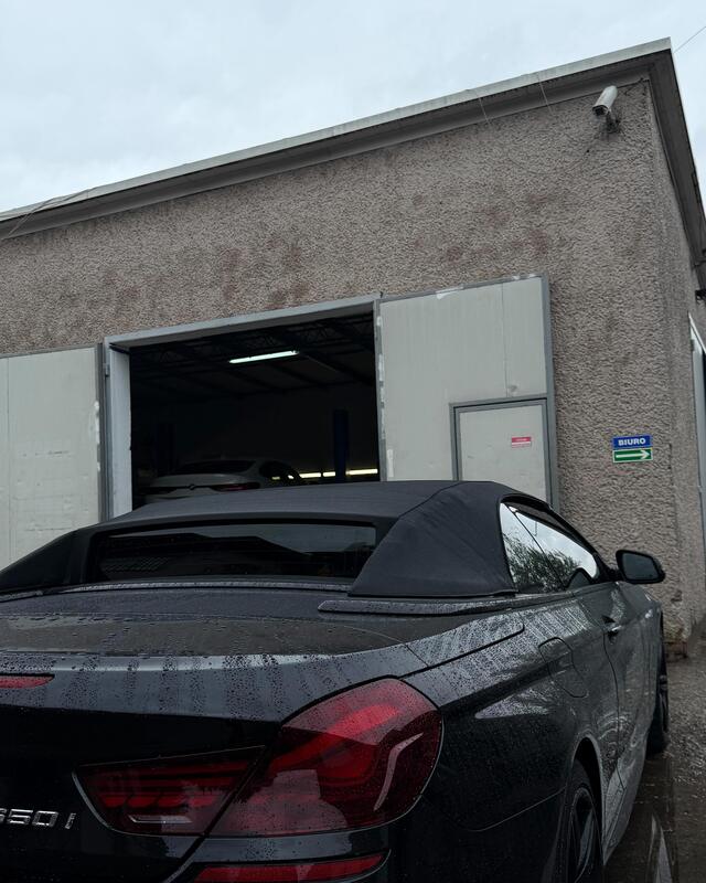 Budynek warsztatu z&nbsp;otwartą bramą, przed nim czarne BMW kabriolet.
