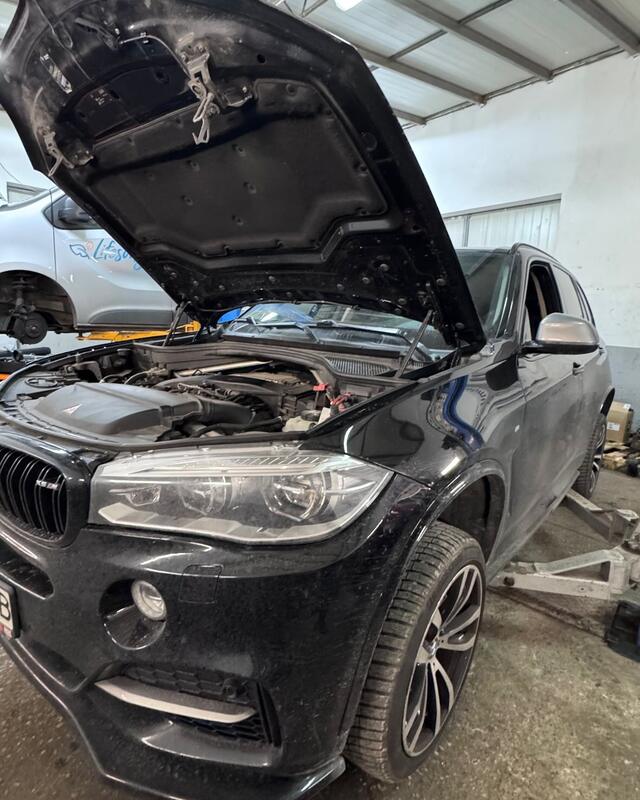 Czarne BMW X5 z&nbsp;otwartą maską na stanowisku w&nbsp;warsztacie.